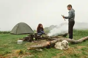 Couple making campfire in the mountains on foggy weather.