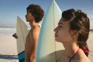 Thoughtful couple standing on the beach with their surfboards and watching the waves at beatch