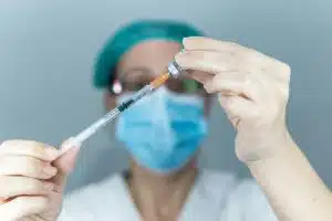 Close up of a nurse with face mask filling syringe with medication of a vial, health care and vaccin