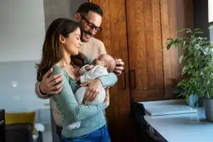 Portrait of young happy man and woman holding newborn cute babe dressed in white unisex clothing.