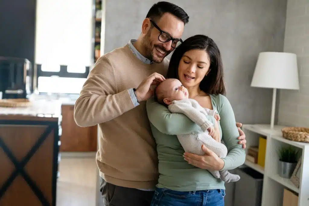 Portrait of young happy man and woman holding newborn cute babe dressed in white unisex clothing.